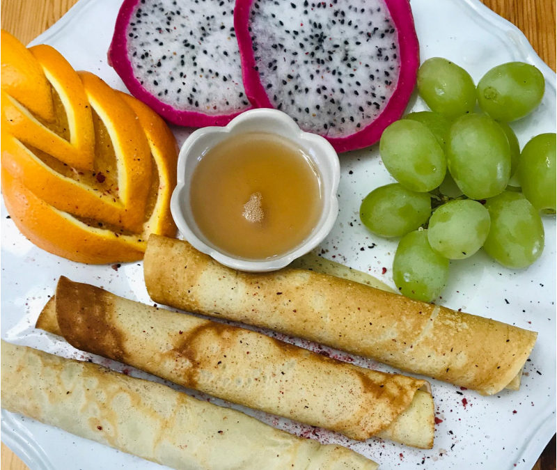 Plate of coconut crepes with grapes, oranges, dragon fruit and maple syrup